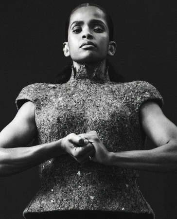 Low angle monochrome portrait of a woman wearing a textured high neck structured top with clasped hands