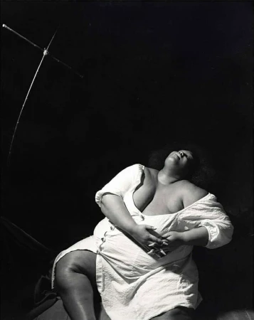 Plus size black woman in white dress seated against dark background with abstract structure by Xavier Scott Marshall