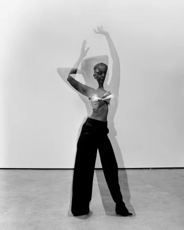 Black and white multiple exposure photograph of a woman wearing a structured top and dark trousers against a light background.