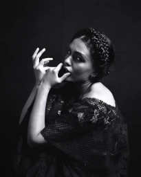 Monochrome portrait of a woman with braided hair wearing a black lace dress against a dark background, photographed by Xavier Scott Marshall.