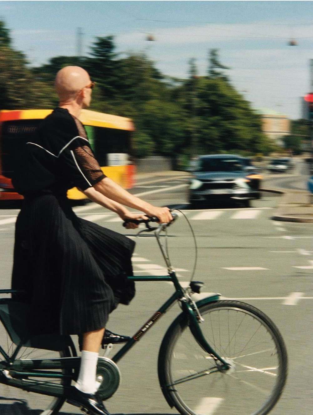 A person riding a bicycle at a crosswalk with a yellow bus and a black car in the background on a sunny day in an urban environment.