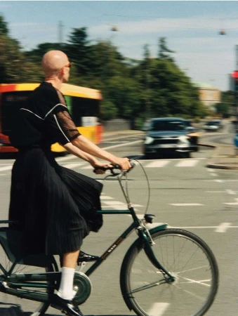 A person riding a bicycle at a crosswalk with a yellow bus and a black car in the background on a sunny day in an urban environment.