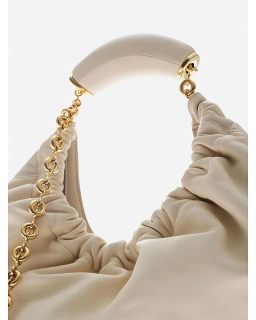 Close-up of a beige leather hobo bag with a gold chain strap and a curved handle, set against a bright white background, fashion accessory.