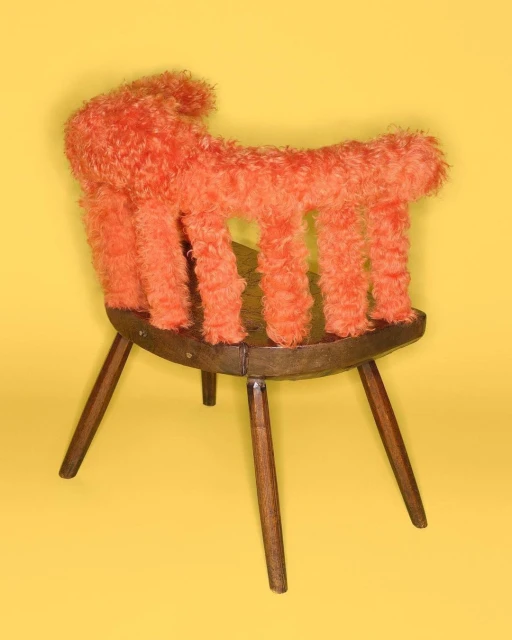 Wooden chair with orange faux fur upholstery, presented on a yellow background in a studio environment.