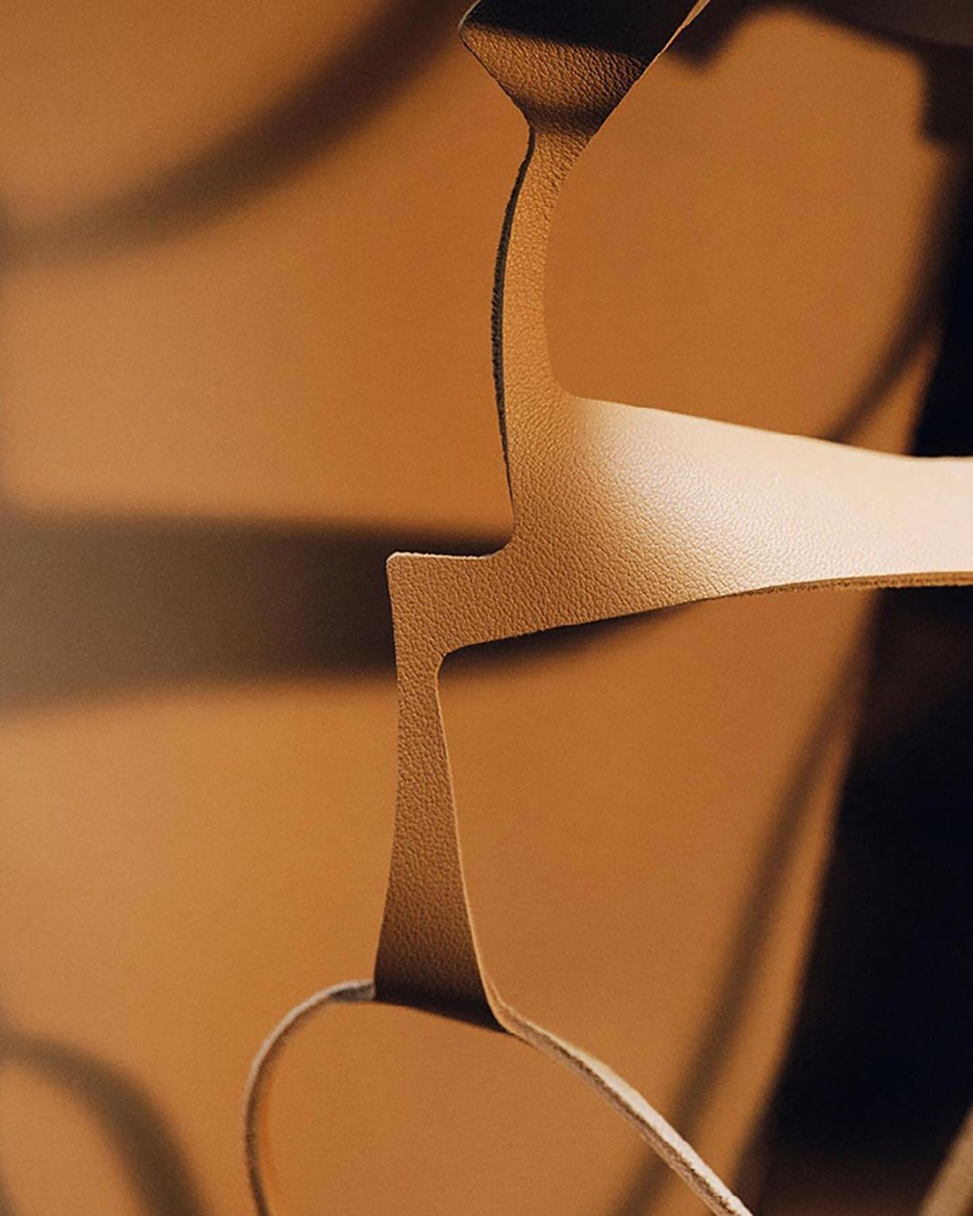 Close-up of a geometric design featuring tan-colored leather cutouts with sharp angles and curves against a background in similar colors.