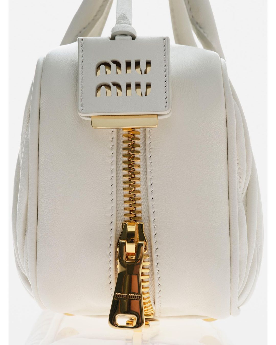 Close-up studio shot of a white leather Miu Miu handbag with a gold zipper and logo tag. Fashion product photography, isolated on white.