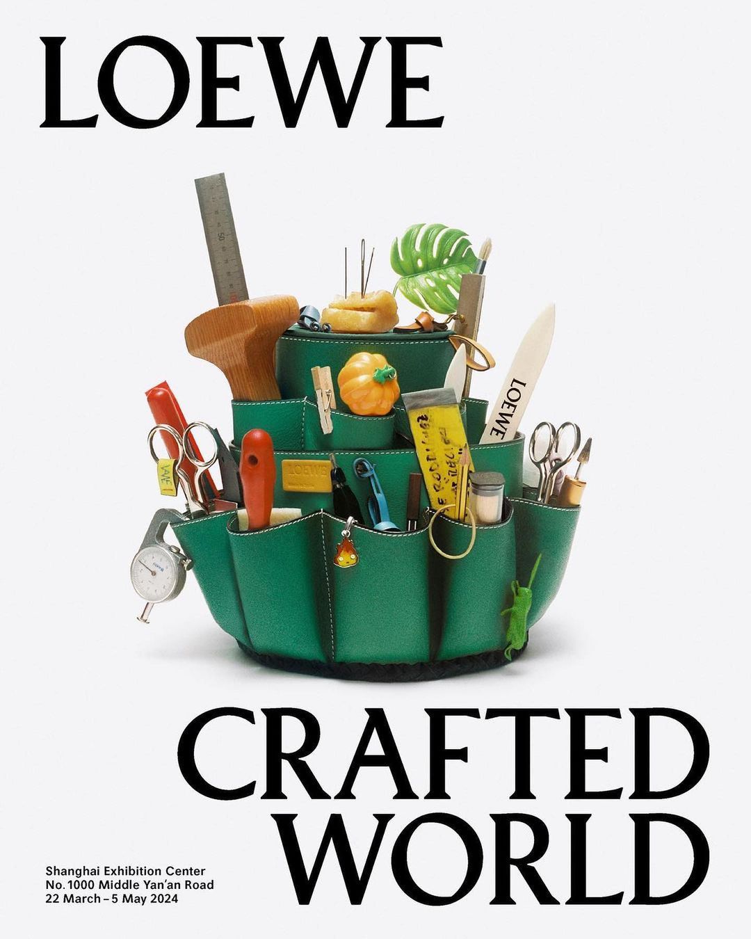 Still life studio photography of a green leather crafting organizer filled with tools and Loewe branded objects on a white background.