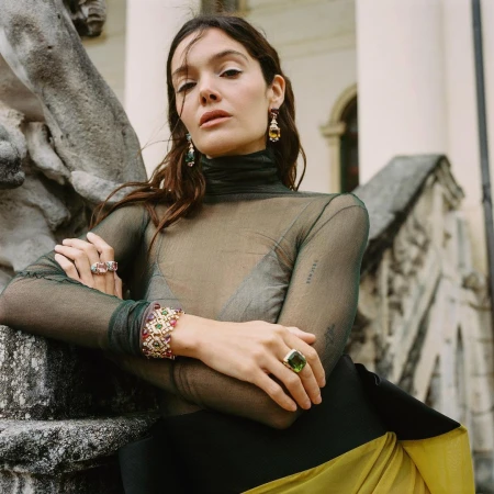 Woman in green sheer turtleneck top and yellow skirt leaning against stone architectural stairs outdoors.