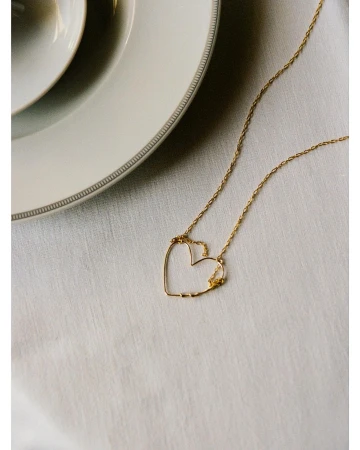 Gold necklace with a heart-shaped pendant on a white tablecloth next to white ceramic plates, showcasing jewelry and table setting.