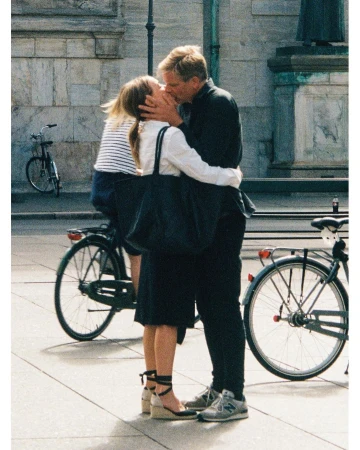 A man and woman kissing on a public square outdoors next to parked bicycles, photographed by Yago Castromil.