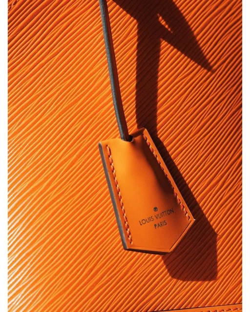 Close-up of an orange textured leather accessory with a black loop attached to a leather Louis Vuitton branded tag.