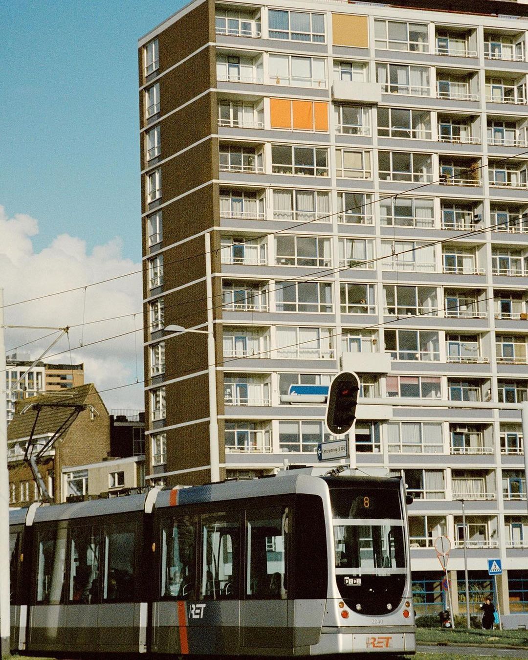 Modern tram in city with a tall apartment building and blue sky. Public transportation and urban architecture create a clean cityscape.