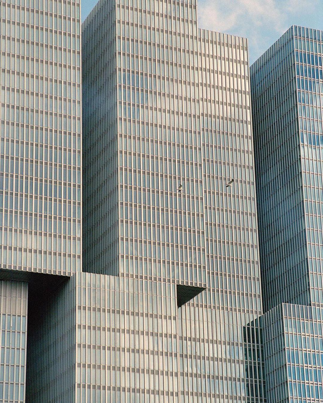 Exterior view of modern architecture featuring a cluster of interconnected, reflective glass skyscrapers against a clear blue sky.
