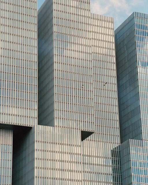 Exterior view of modern architecture featuring a cluster of interconnected, reflective glass skyscrapers against a clear blue sky.