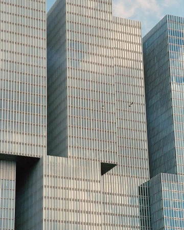 Exterior view of modern architecture featuring a cluster of interconnected, reflective glass skyscrapers against a clear blue sky.