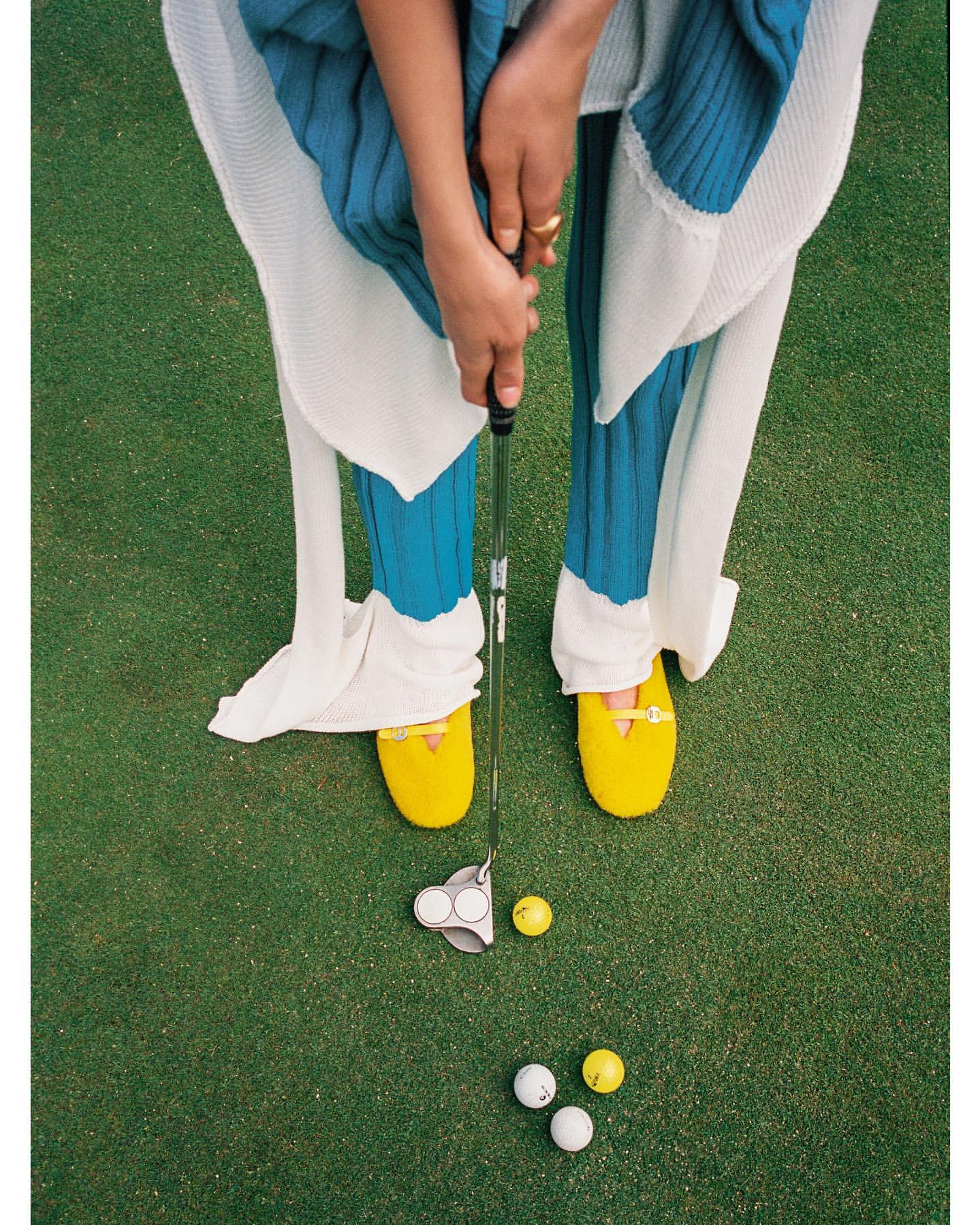 Overhead view of a woman on a golf course holding a golf club with golf balls on the green grass in bright yellow shoes.