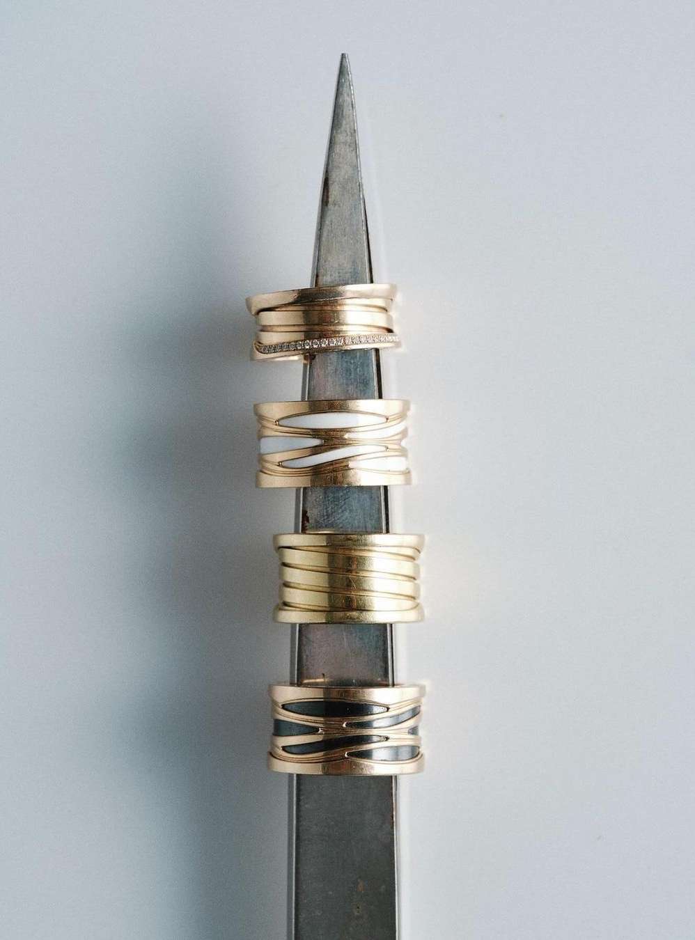 Close-up of four stacked gold rings with varying designs on a metal display stand against a plain white background, jewellery product.