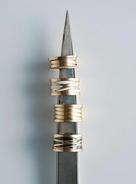 Close-up of four stacked gold rings with varying designs on a metal display stand against a plain white background, jewellery product.