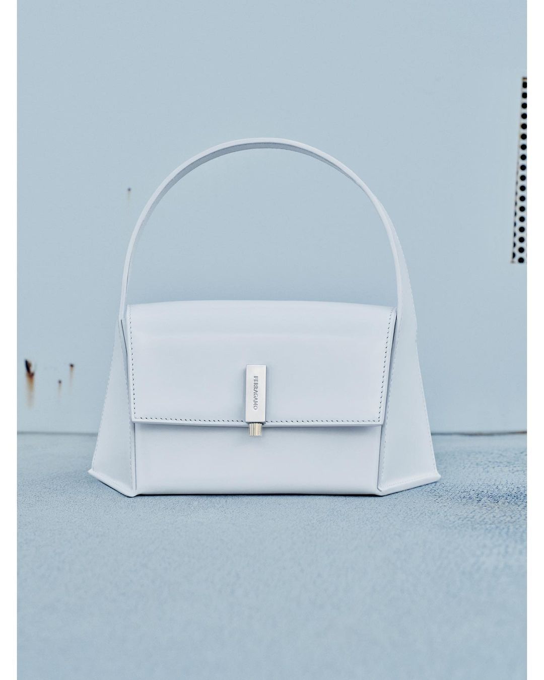 Light blue leather purse with a silver clasp and handle in a studio setting featuring a light blue wall and floor.