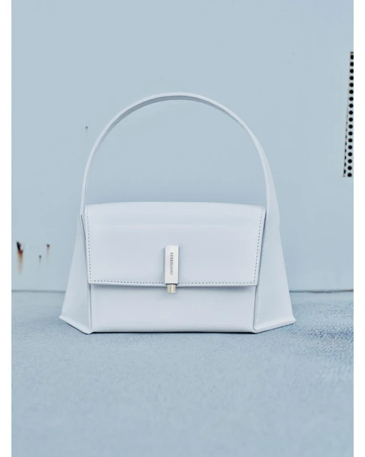 Light blue leather purse with a silver clasp and handle in a studio setting featuring a light blue wall and floor.