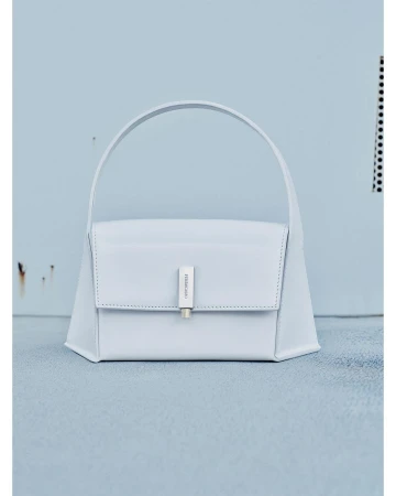 Light blue leather purse with a silver clasp and handle in a studio setting featuring a light blue wall and floor.