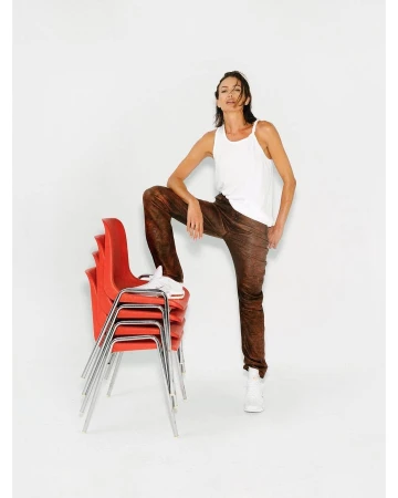 An adult female is posing indoors in a white tank top and brown pants, with one leg resting on a stack of red chairs.