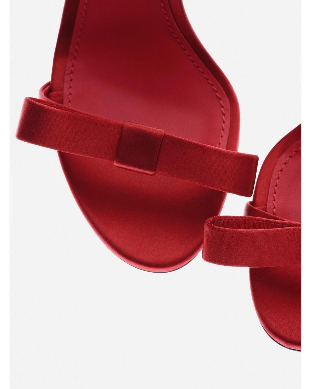 Close-up shot of a pair of elegant red satin high-heeled sandals. The shoes feature ankle straps with bow details.