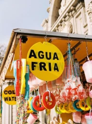 Bright yellow Agua Fria sign hanging on a street vendor stall filled with colorful toys and candy in Madrid