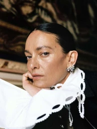 Close-up portrait of a woman resting her chin on her hand, wearing a white ruffled collar and dark jacket.
