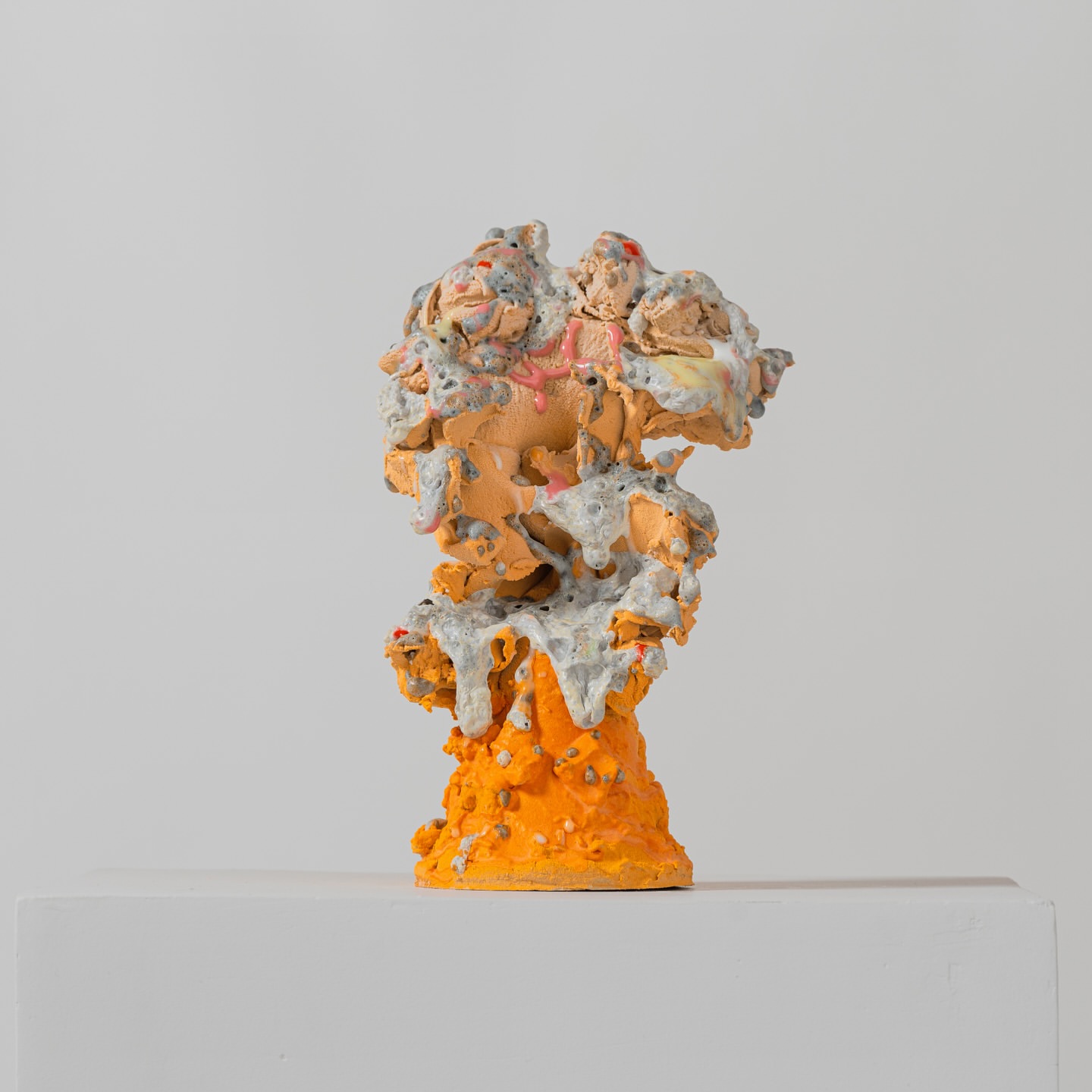 Abstract art sculpture in shades of orange and gray with a textured surface, set against a plain white background.