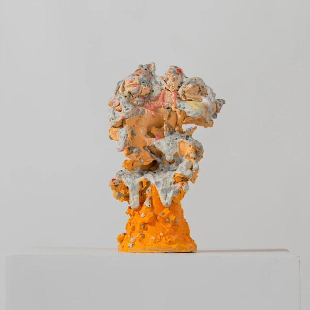 Abstract art sculpture in shades of orange and gray with a textured surface, set against a plain white background.