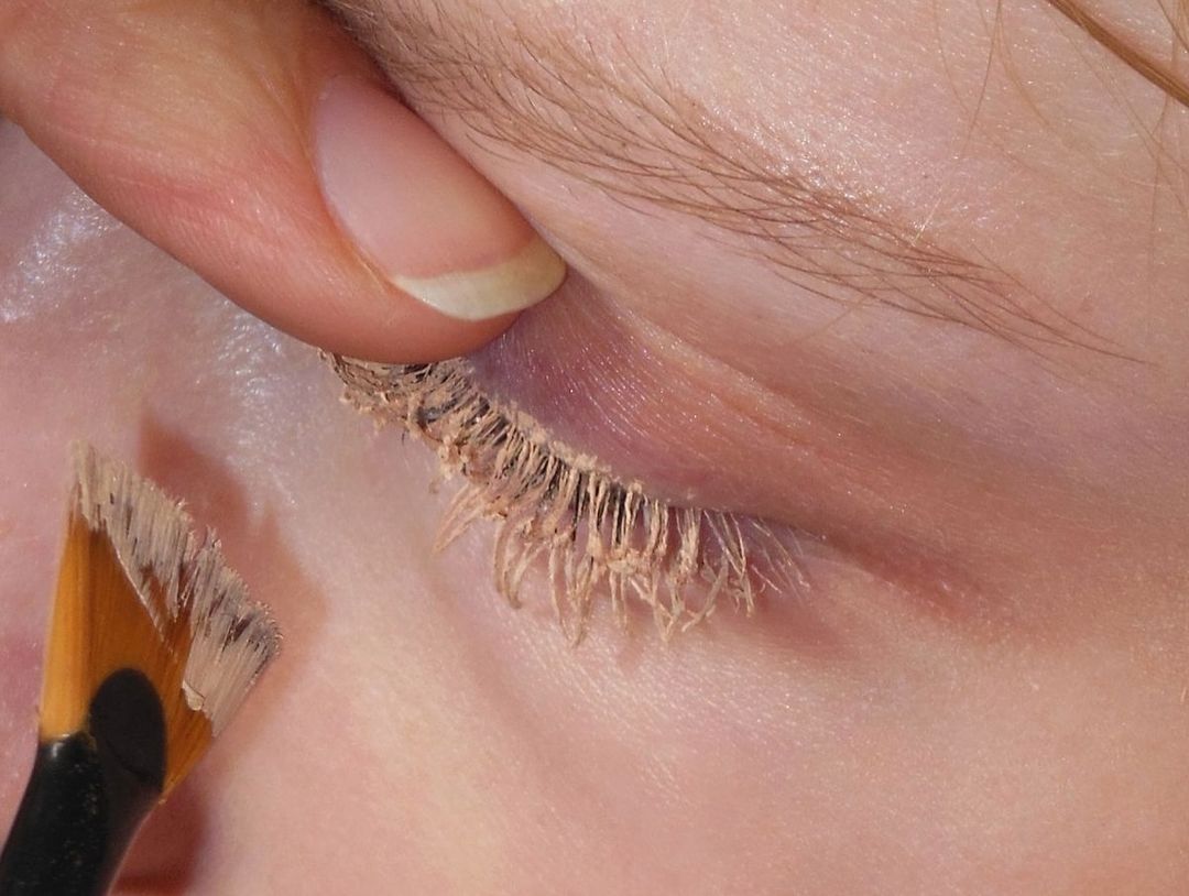 Close-up of a person applying makeup to their eyelashes with a makeup brush, highlighting beauty and cosmetic application process.