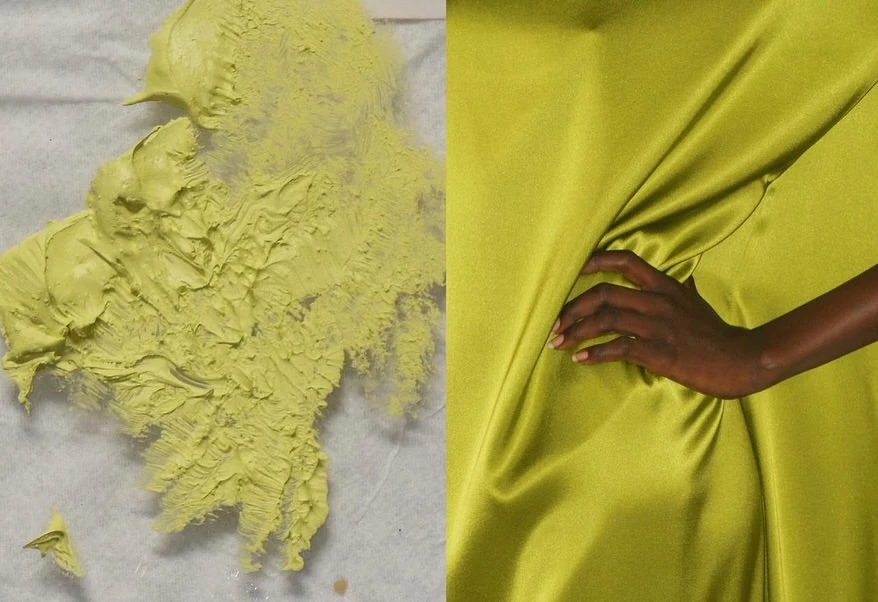 Close-up of yellow-green textured paint and draped fabric, an adult woman's hand peeks from the shiny textile folds.