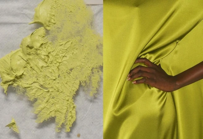 Close-up of yellow-green textured paint and draped fabric, an adult woman's hand peeks from the shiny textile folds.