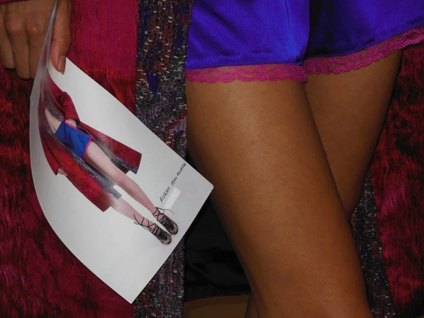 Woman's legs wearing purple lace-trimmed shorts, holding a fashion image with a model wearing a similar outfit and platform shoes.