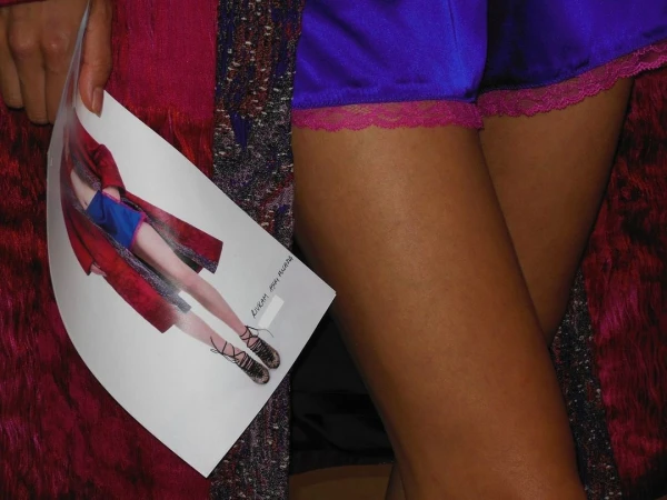 Woman's legs wearing purple lace-trimmed shorts, holding a fashion image with a model wearing a similar outfit and platform shoes.