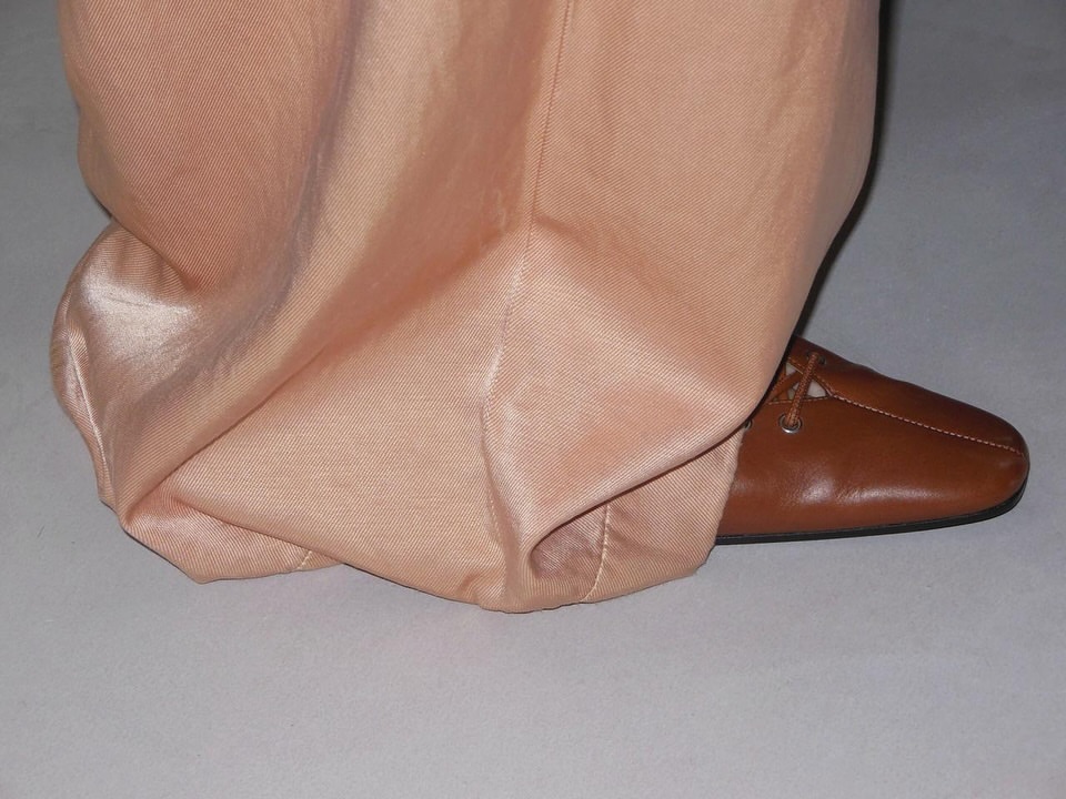 Close-up of peach colored, draped fabric of pants with brown leather loafer-style shoe.  Bottom clothing and footwear.  