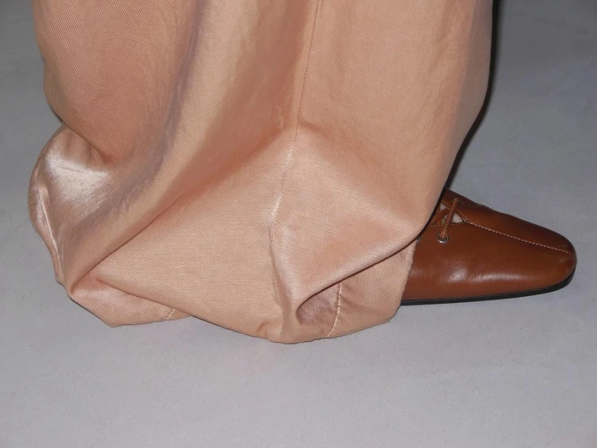 Close-up of peach colored, draped fabric of pants with brown leather loafer-style shoe.  Bottom clothing and footwear.  