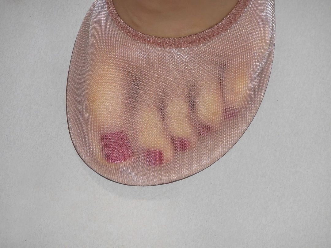 Close-up of a foot wearing a sheer, nude-colored sock, showing painted toenails and the sock's textured fabric against a neutral background.