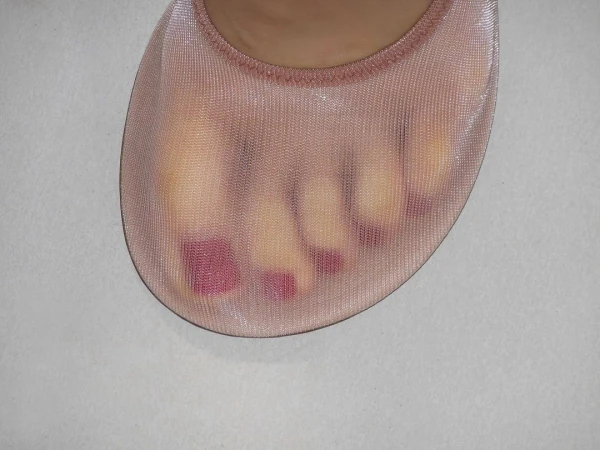 Close-up of a foot wearing a sheer, nude-colored sock, showing painted toenails and the sock's textured fabric against a neutral background.