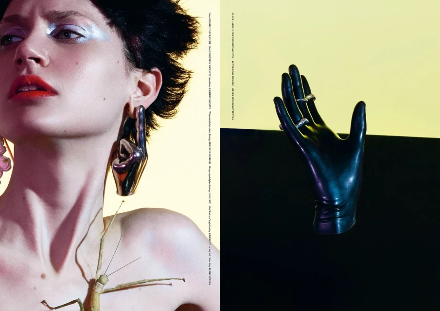 Fashion editorial shot featuring a woman with a bug on her chest and hand-shaped earrings alongside a sculptural hand with rings on fingers.
