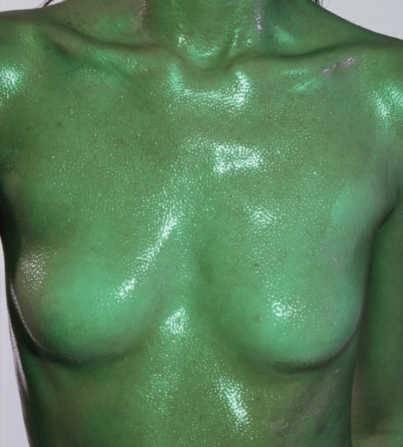 Torso of a female adult covered in a green, shimmery substance against a plain light background in a close-up shot.