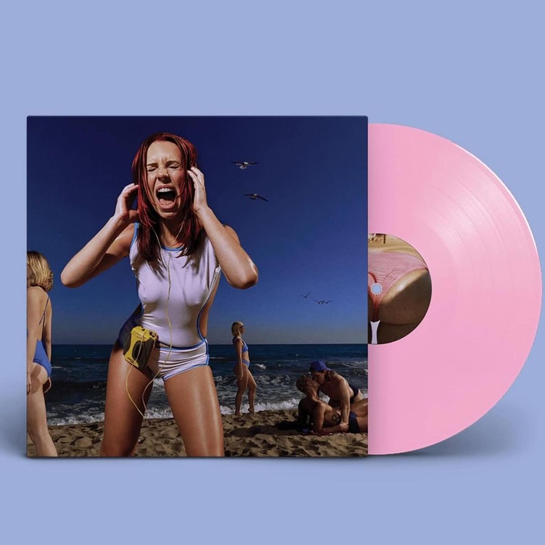 Record cover featuring woman screaming with a vintage music player on the beach. Pink vinyl record is set against a blue background.