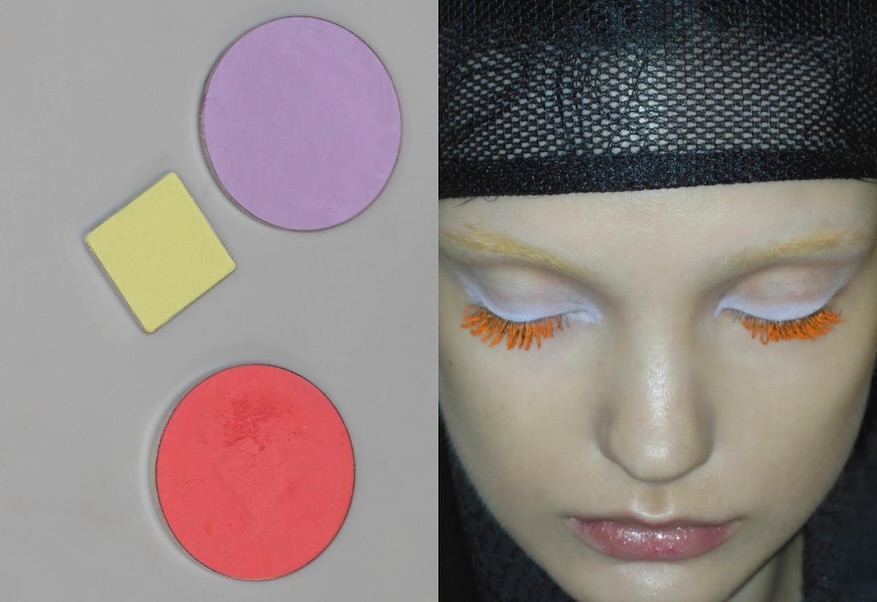 Close-up of a model's face with colorful makeup and makeup pallets in shades of lavender, yellow, and red on a gray background.