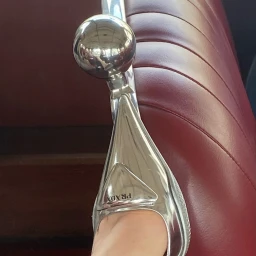 Close-up of a glossy silver metallic Prada shoe resting against a deep red tufted leather seat.