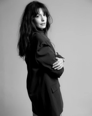 Anne Hathaway with dark hair and bangs in a black blazer, captured in a monochrome portrait by Yana Yatsuk.