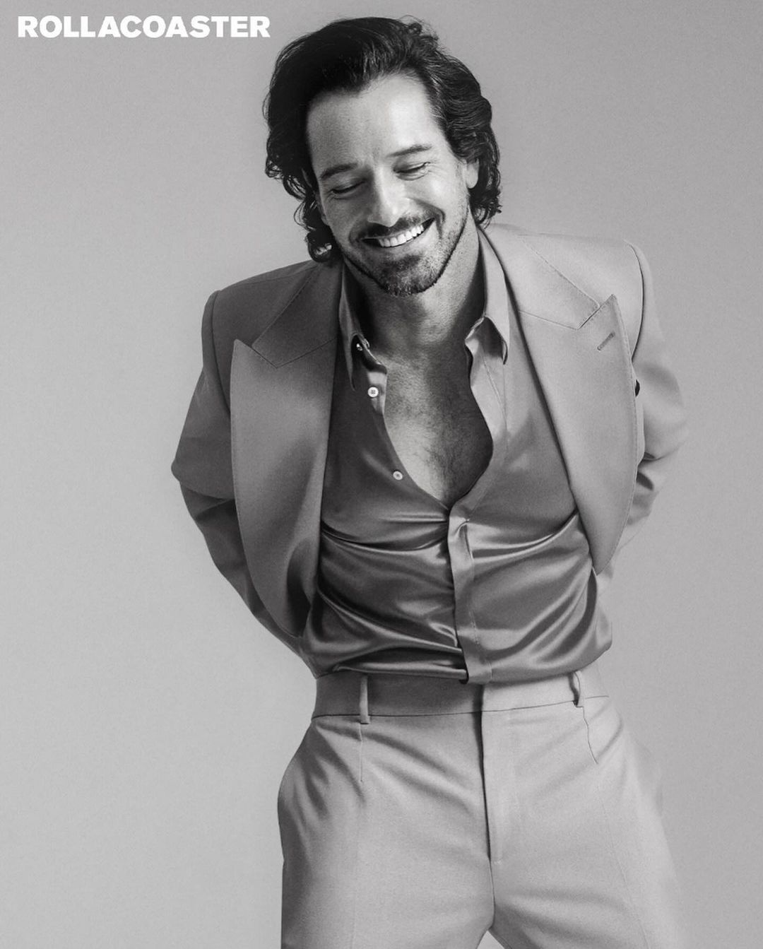 Black and white portrait of an adult male in a suit, smiling, with curly dark hair, in an indoor setting with magazine logo.