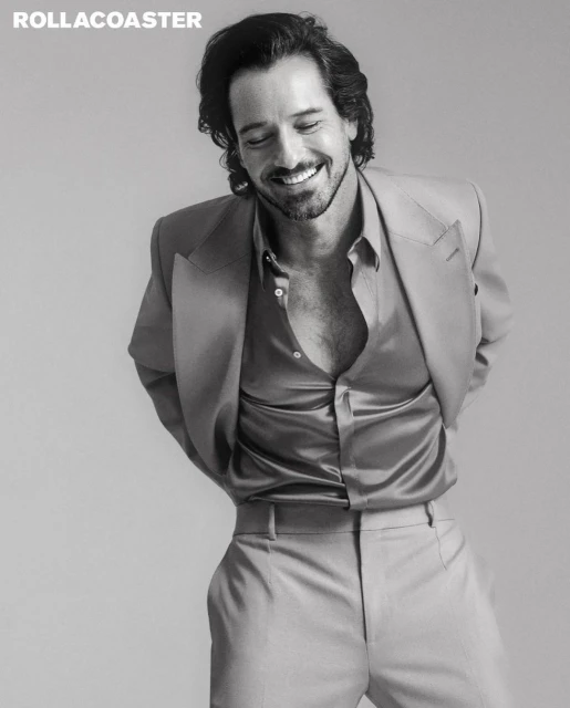 Black and white portrait of an adult male in a suit, smiling, with curly dark hair, in an indoor setting with magazine logo.