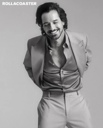 Black and white portrait of an adult male in a suit, smiling, with curly dark hair, in an indoor setting with magazine logo.