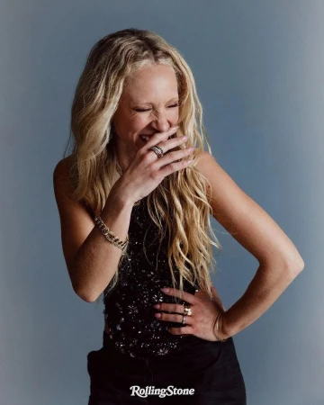 Blonde woman laughing with hand covering mouth wearing a dark sequined top against a grey backdrop photographed by Yana Yatsuk